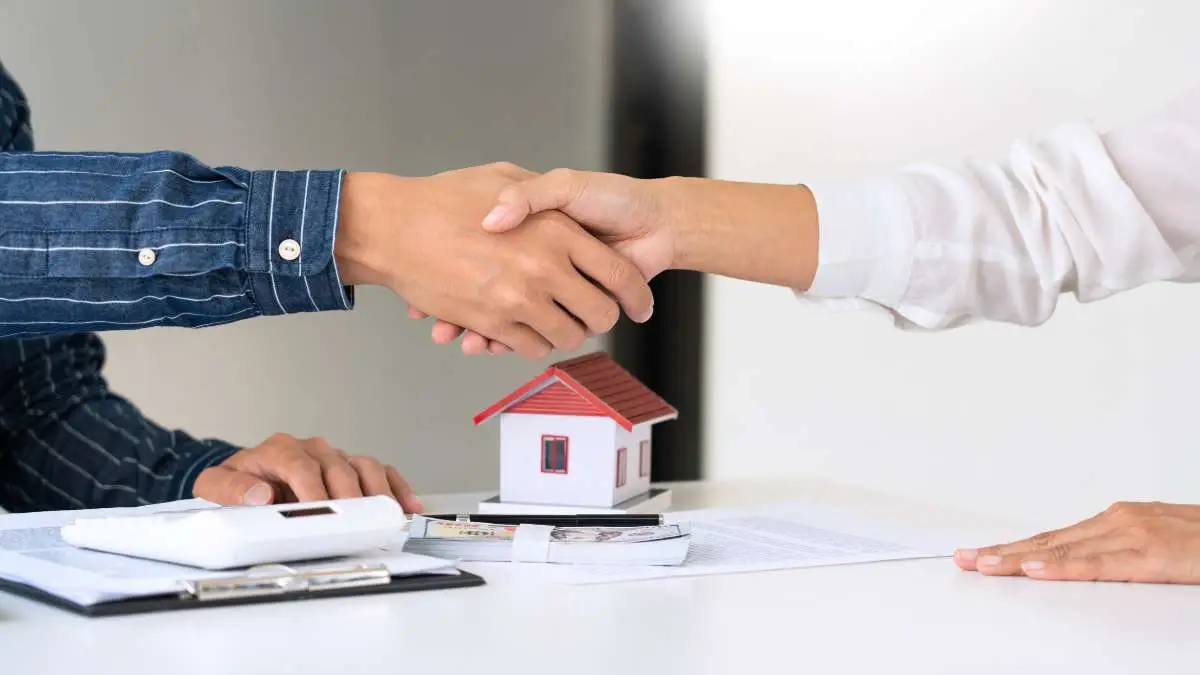 Un agent immobilier serre la main d'un client avec une petite maison en modèle sur la table